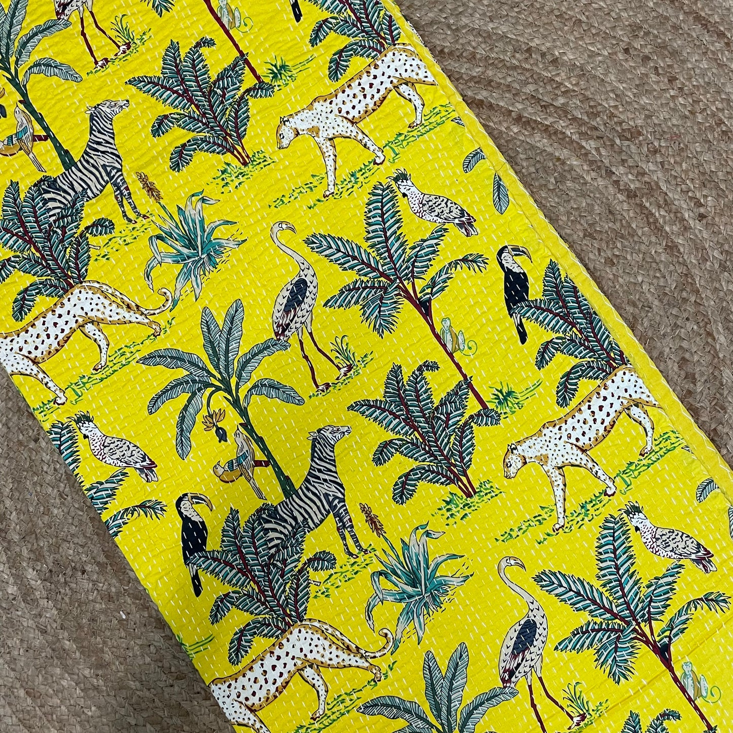 Fabric with a jungle-themed pattern featuring animals and plants on a yellow background.