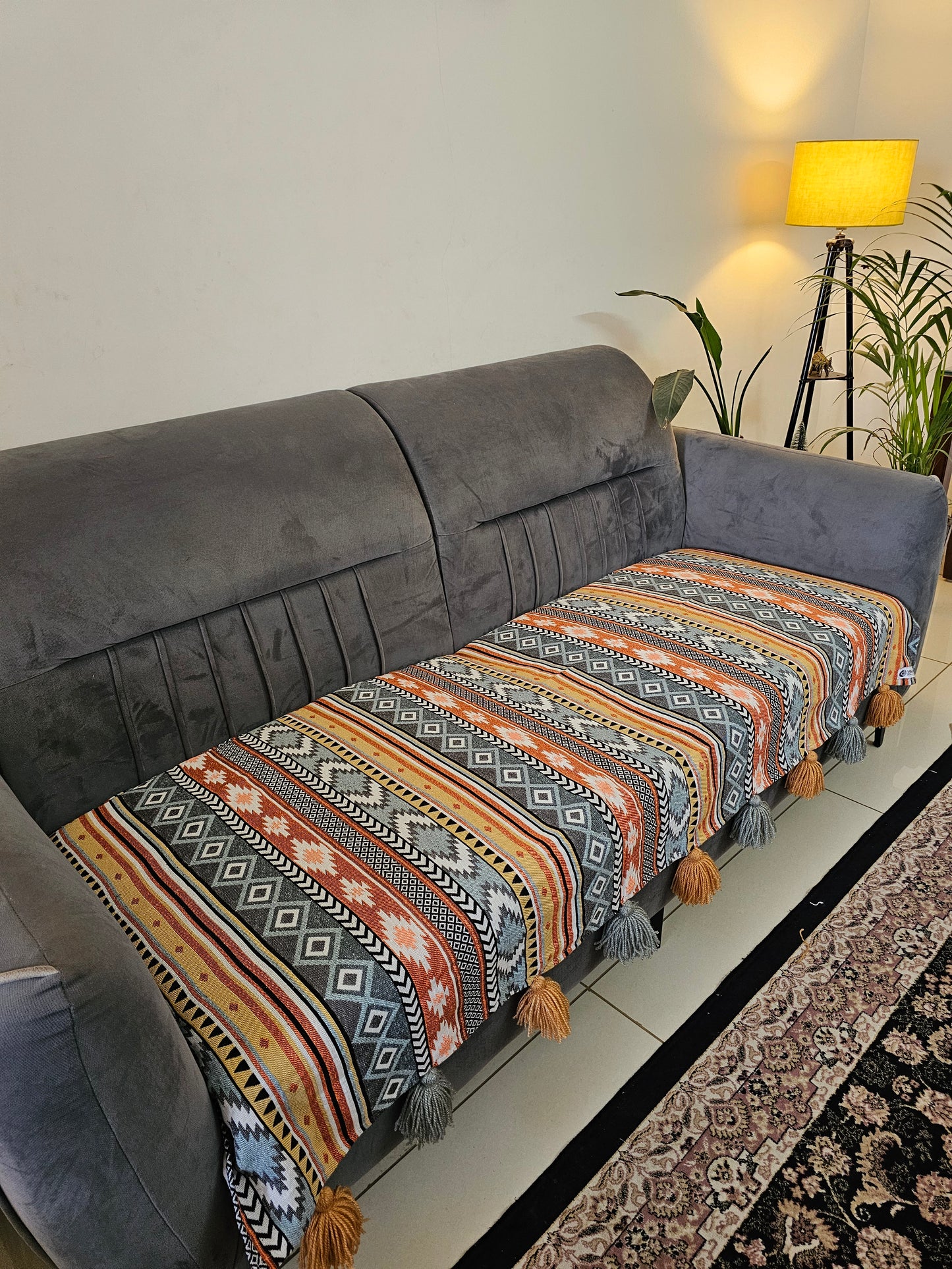 Decorative pillow with geometric pattern on a gray sofa in a room with a rug and lamp.