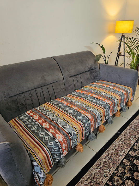 Decorative pillow with geometric pattern on a gray sofa in a room with a rug and lamp.